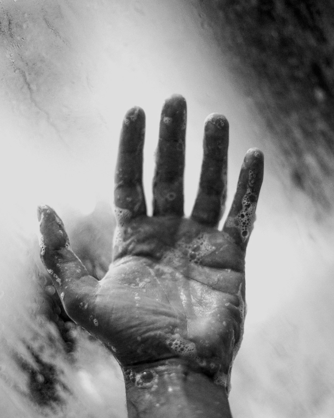 Close-up hand and flowing water seen through a misted shower screen.